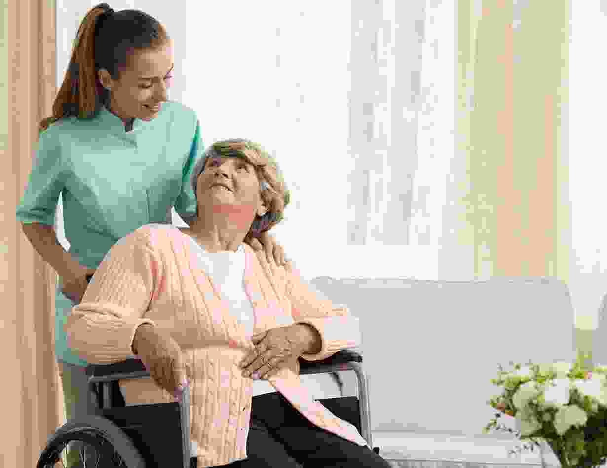 Une infirmière accompagne une résidente en fauteuil roulant dans un salon lumineux