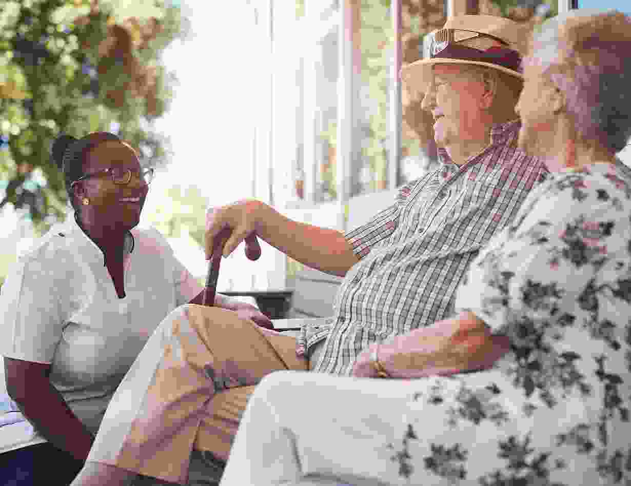 Une soignante discute avec deux résidents assis près d’une grande fenêtre